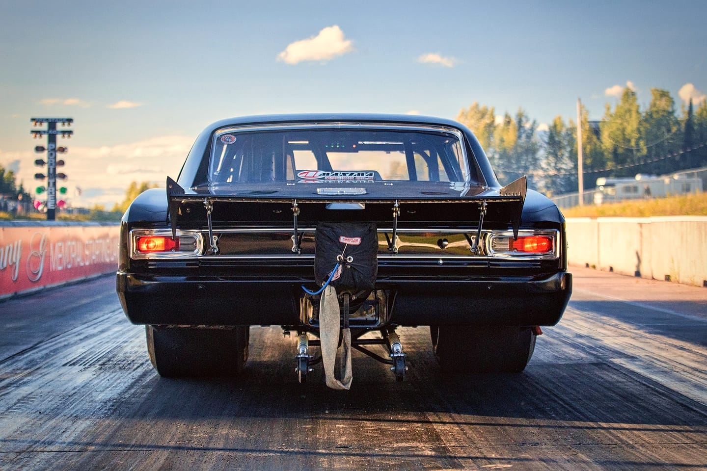 Rear view of a black drag car staged on the starting line, looking down the strip.