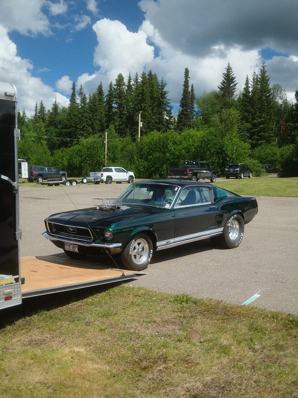 A classic Ford Mustang fastback beside its open trailer in the paddock at NITRO Motorsports Park.